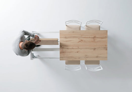 Persona abriendo el extensible de una mesa de cocina color roble con estructura blanca y sillas blancas a juego con asiento color Crema.